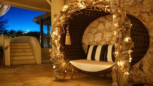 A cozy, circular wooden bench with a cushioned seat and striped pillow, surrounded by string lights and rustic decor, set against a stone wall. - La Casa Panacea Okinawa Resort (Onna)