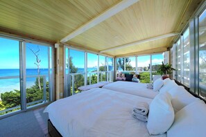 Amplia habitación con techo de madera y ventanas grandes que dan a una vista del océano.