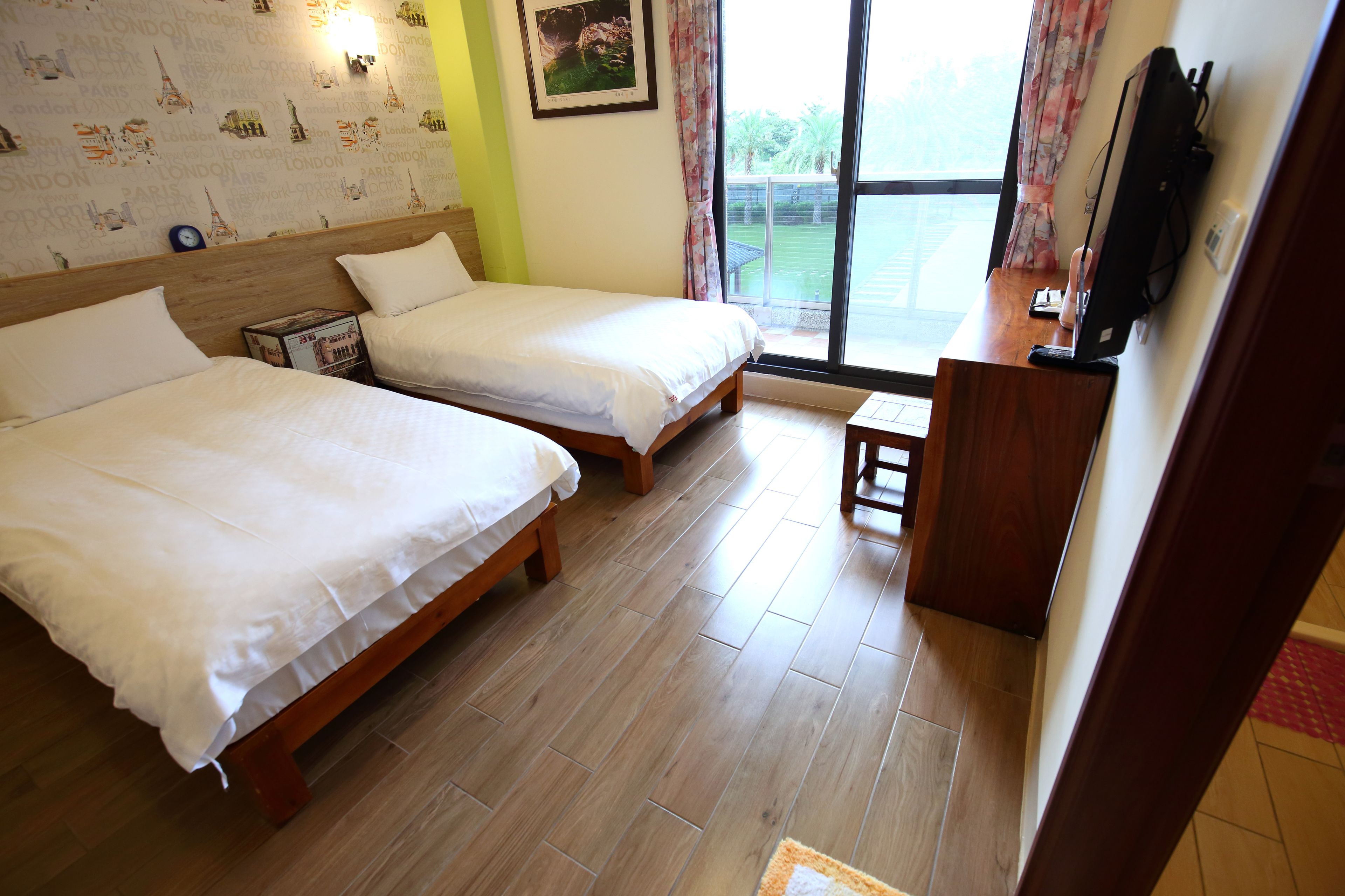 A hotel room with two beds, a wooden floor, a TV, and a window with curtains.