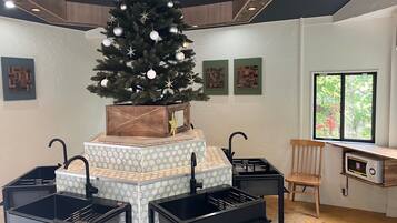 A modern kitchen with a central island, black bar stools, a wooden chair, a Christmas tree, and a window with a view.
