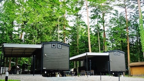 A campground with two small, gray cabins with attached porches, surrounded by dense forest.