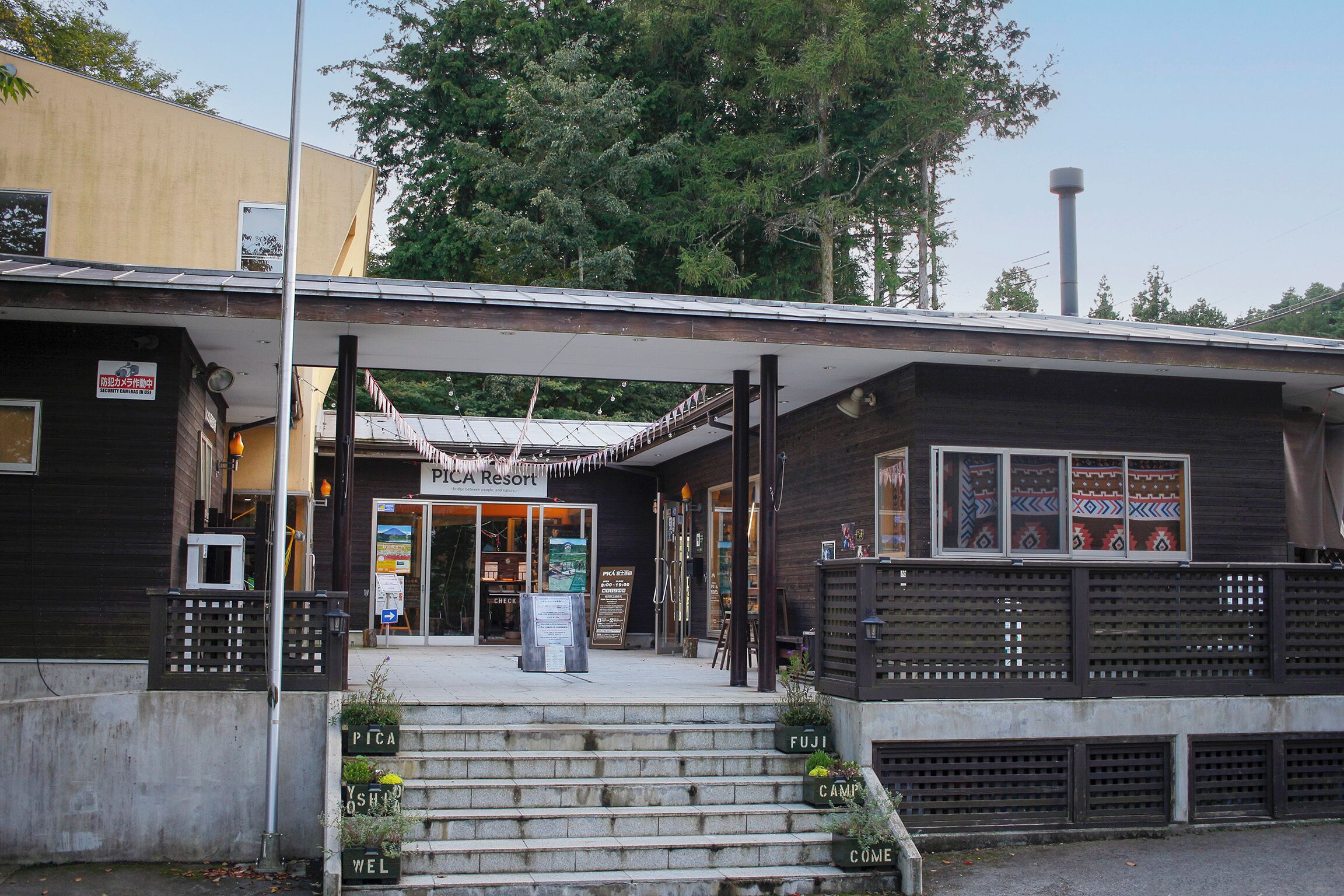 A wooden building with a covered entrance, steps leading up to it, and signs indicating "PICA" and "FUJI CAMP".