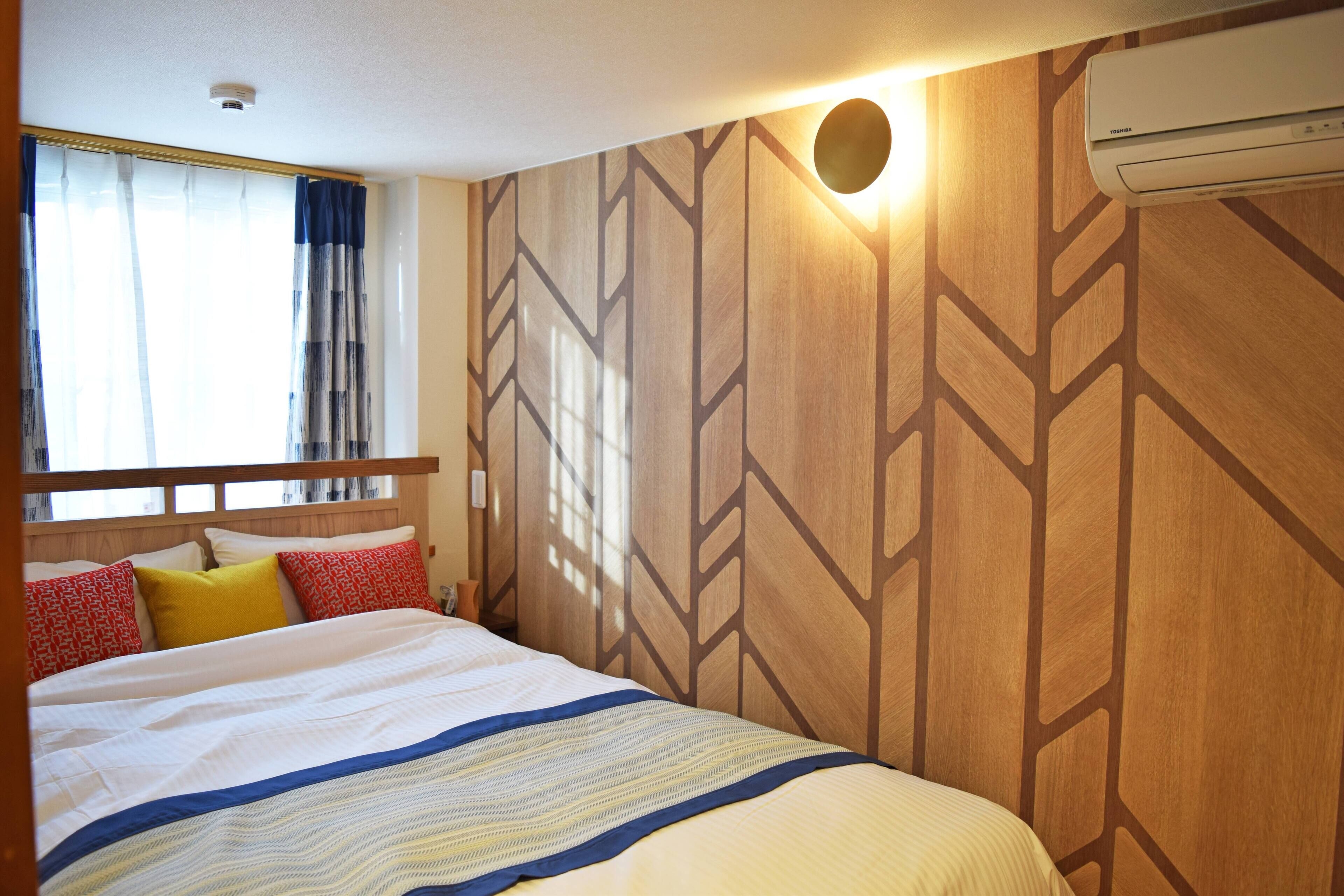 Una habitación de hotel con una cama, paneles de madera en la pared, una ventana con cortinas y un equipo de aire acondicionado.