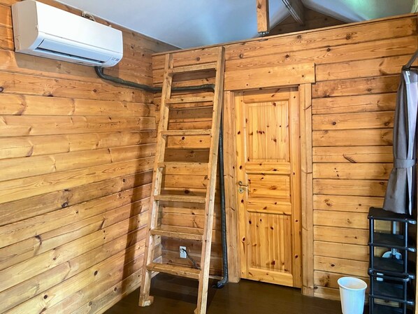 A wooden interior with a ladder, a door, and an air conditioning unit.