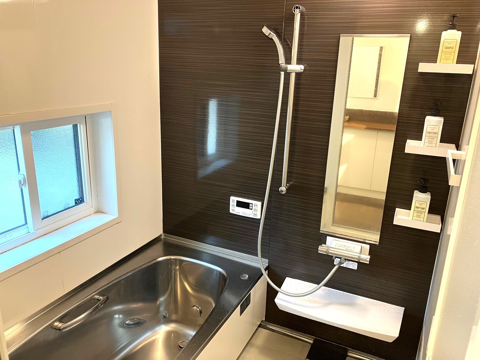 Et moderne badeværelse med en stor vask, en bruser med håndbruser, et spejl og en hylde med toiletartikler.