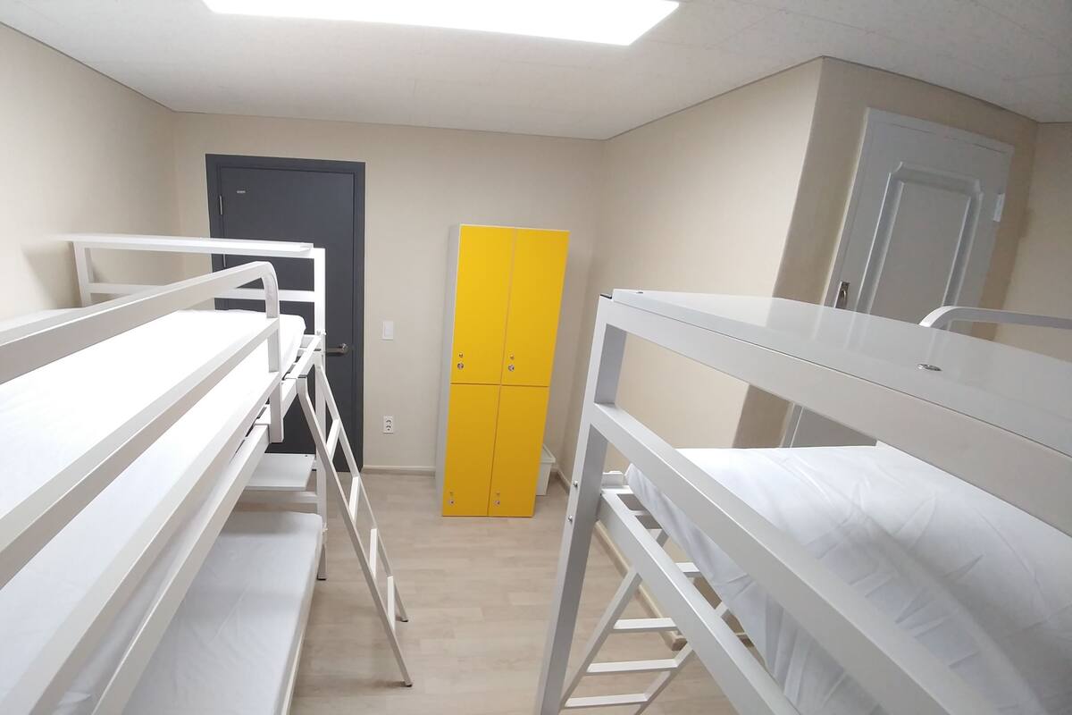 A dormitory room with bunk beds, a wardrobe, and a door.