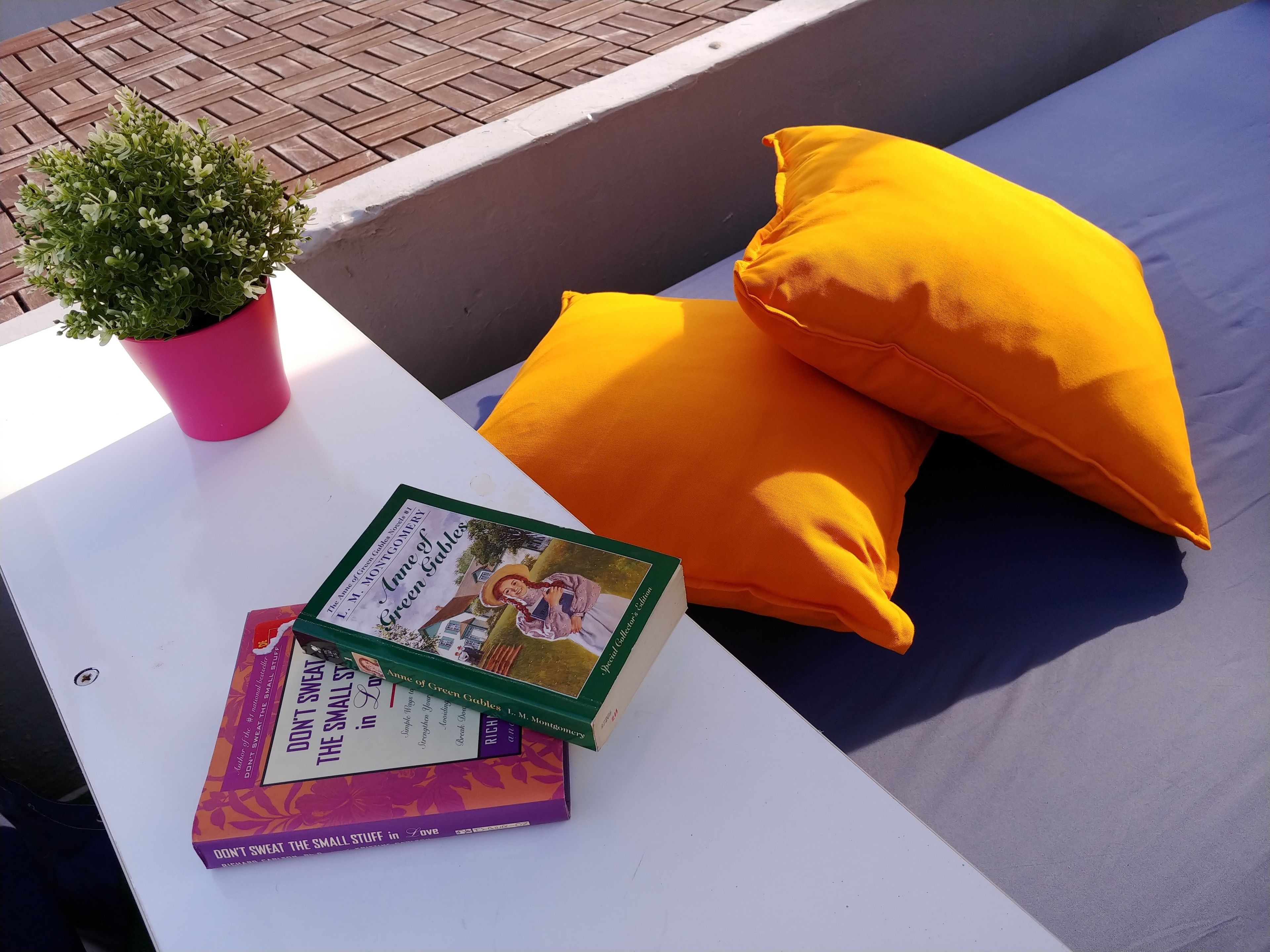 A white table with a potted plant, two books, and a yellow pillow on a blue couch.