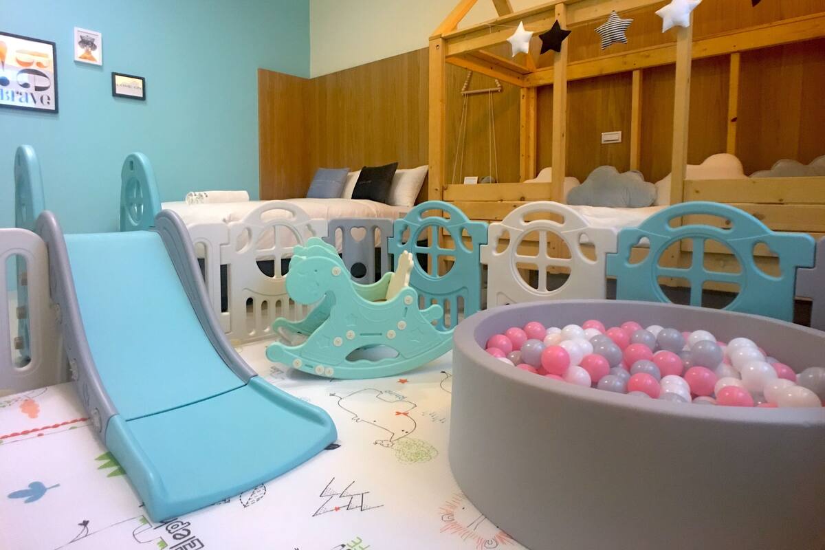 Un área de juegos infantiles con un tobogán, una piscina de pelotas y una casita de madera.