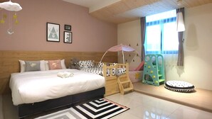 A bedroom with a large bed, a crib, a play area with a toy and a small table, and a window with curtains. - Dio Inn (Hengchun)