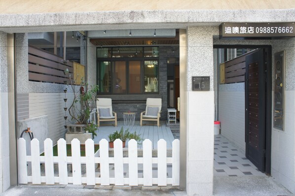 A hotel entrance with a white picket fence, two lounge chairs, and a small table. - Dio Inn (Hengchun)