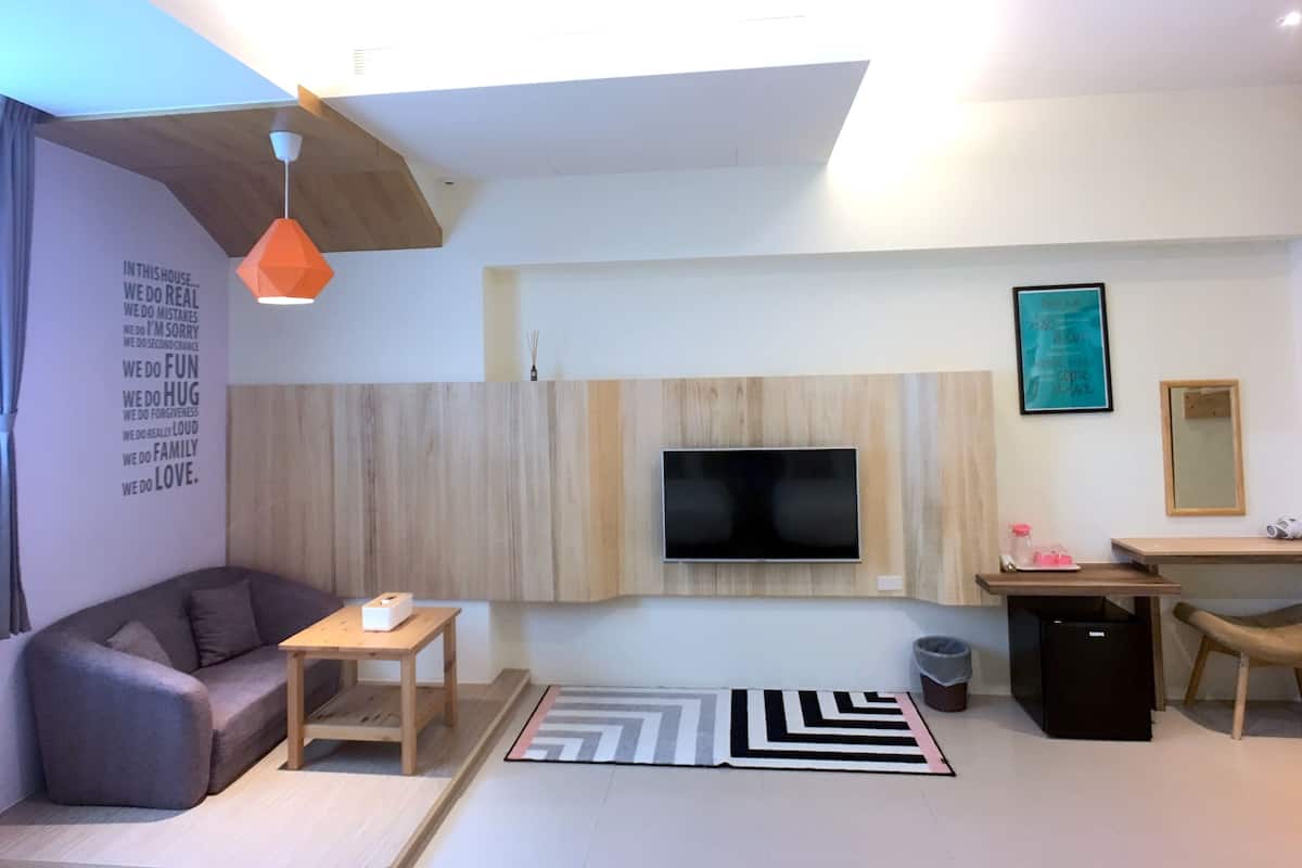 Una sala moderna con un sofá, una mesa de centro, un televisor montado en una pared de madera, un escritorio pequeño con una silla y un cubo de basura.
