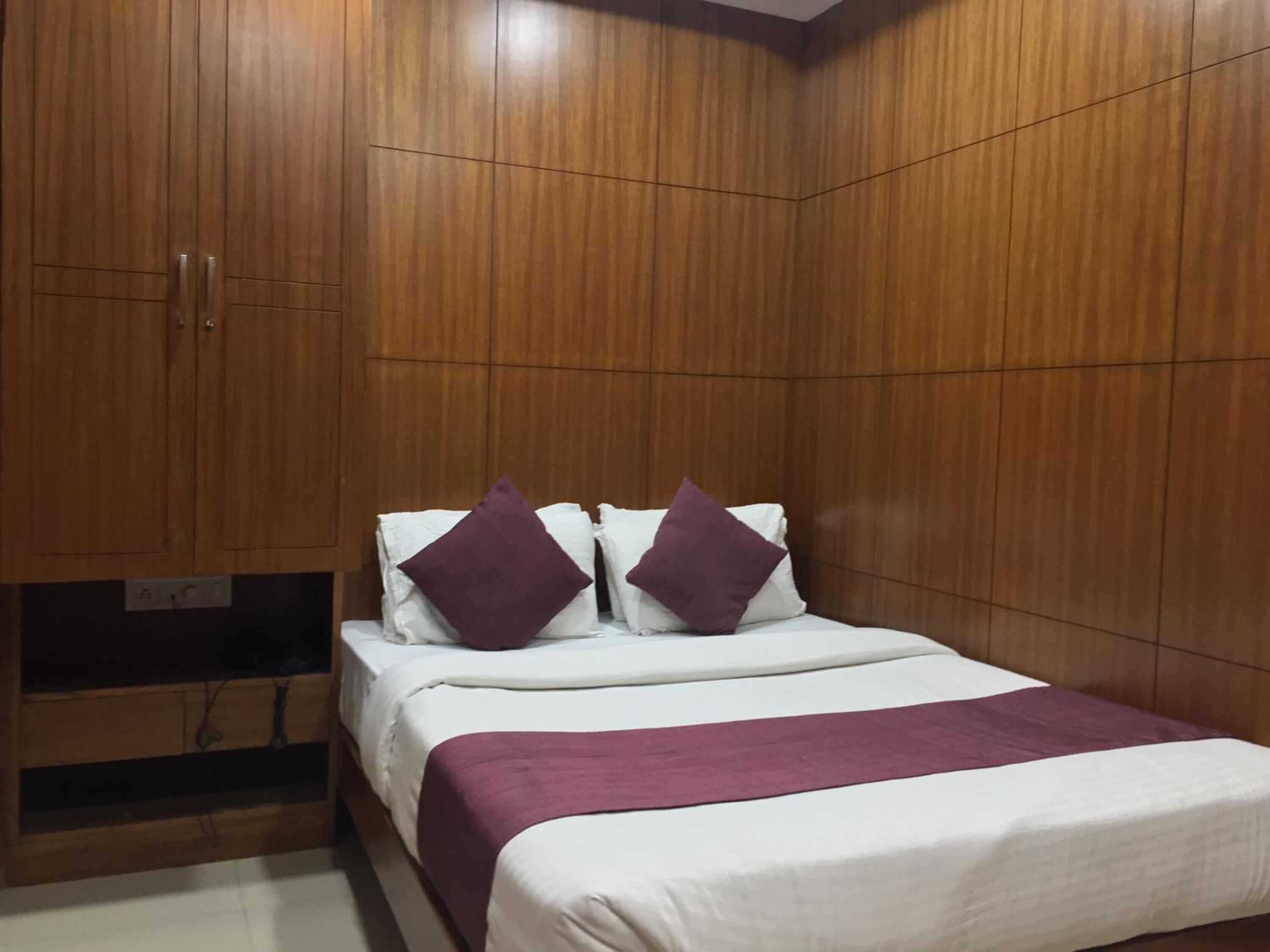 A bedroom with a wooden wardrobe, a bed with white bedding and purple pillows, and a purple throw blanket.