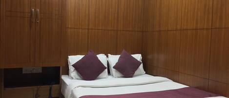 A bedroom with a wooden wardrobe, a bed with white bedding and purple pillows, and a purple throw blanket.