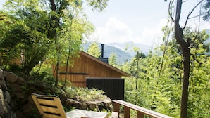 Uma cabana de madeira com parede de pedra, deck de madeira e vista para as montanhas.