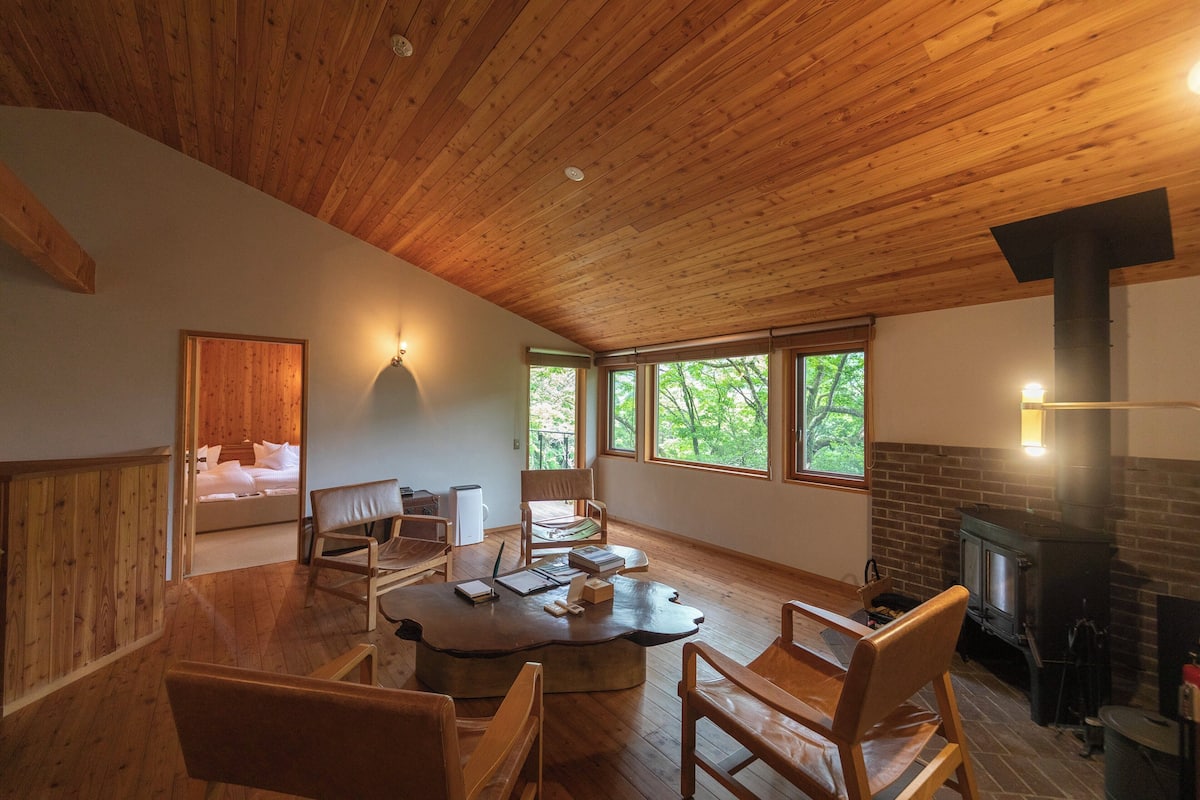 Une pièce chaleureuse avec un plafond en bois, une cheminée, un lit donnant sur un beau paysage et un coin repas avec des chaises et une table.