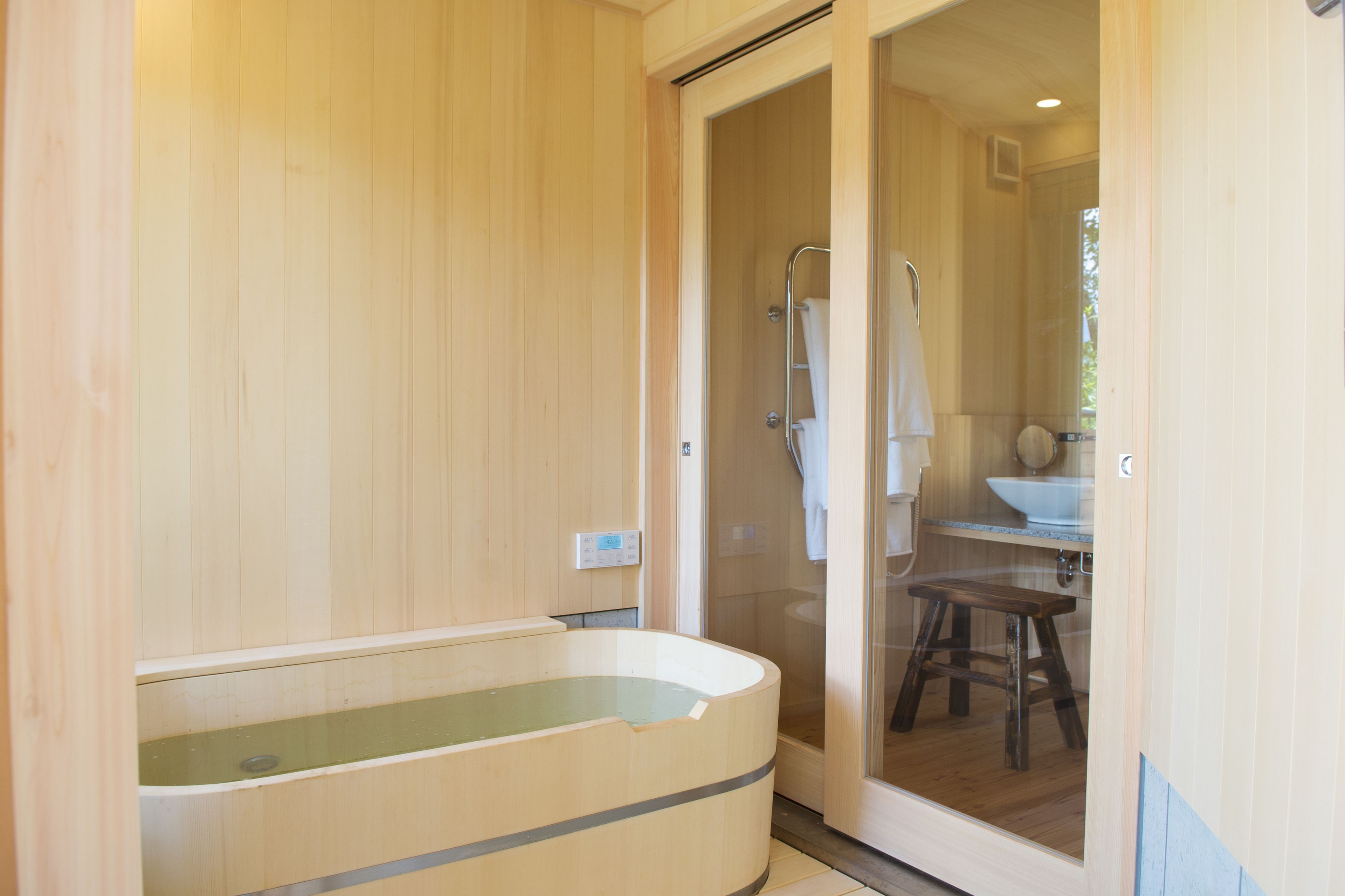 A wooden spa room with a large bathtub, a shower area, and a sink.