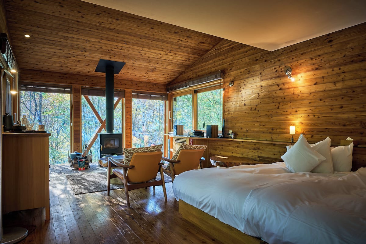 Une chambre confortable dans un chalet, avec un lit, des murs en bois, une cheminée et de grandes fenêtres donnant sur la forêt.