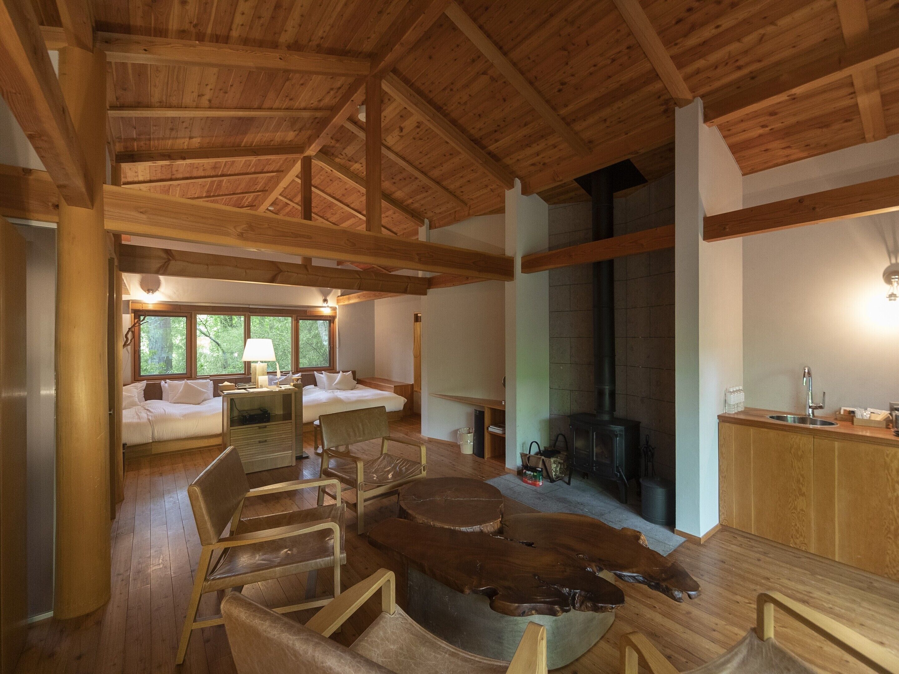 A spacious living area with a high ceiling, wooden beams, a fireplace, and a dining area with a sink.