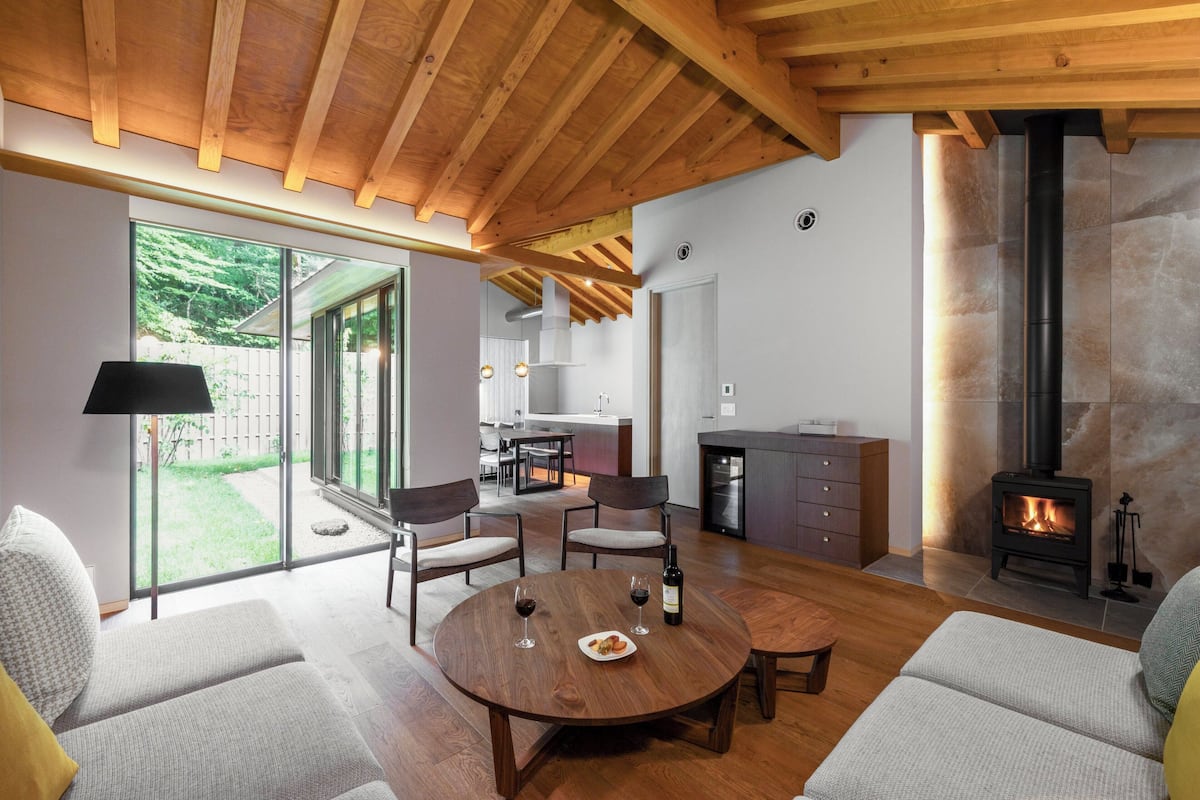 Un salon moderne doté d’une cheminée, de poutres apparentes en bois au plafond et d’un coin repas avec une table ronde et des chaises.