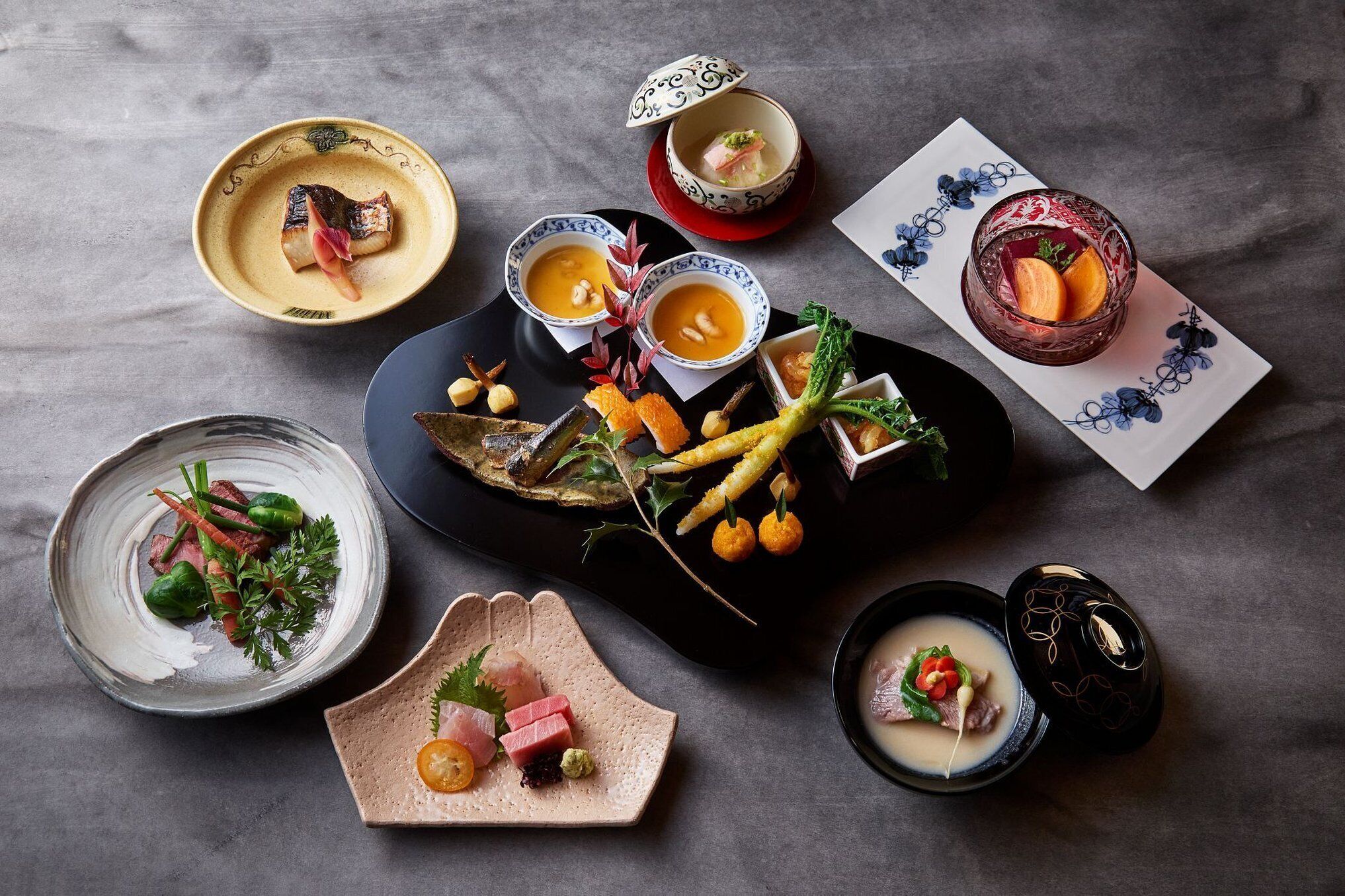 A variety of dishes including sashimi, a bowl of soup, and a plate with vegetables and meat.