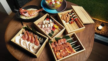 Une table en bois sur laquelle on trouve divers aliments, notamment des crevettes, des brochettes et un saladier de salade de fruits.
