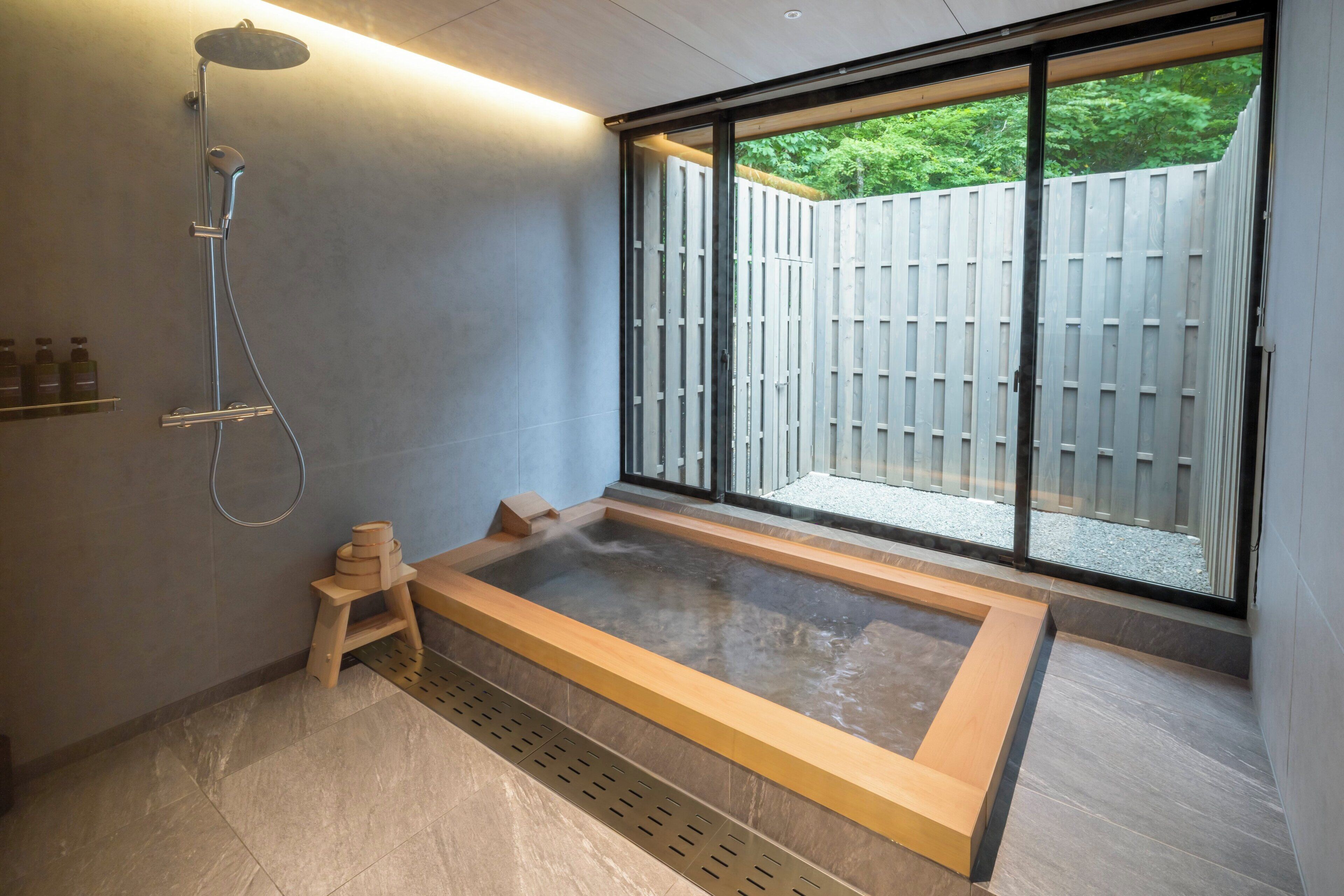 A modern bathroom with a large bathtub, a showerhead, and a small wooden stool.
