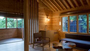 A wooden cabin interior with a kitchen area, a dining table, and a seating area.