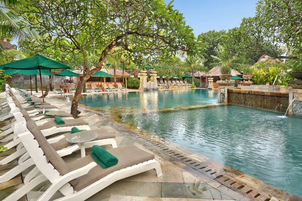 Un área junto a la piscina con sillones de descanso y sombrillas, una piscina cristalina y exuberante vegetación tropical.