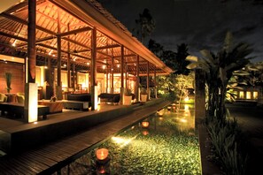 A well-lit outdoor lounge area with a pool, wooden deck, and seating arrangements. - Legian Beach Villas (Legian)
