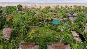 Vista aérea de un resort con piscina rodeada de palmeras, una playa con sombrillas y una vista despejada del océano.