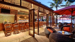 Zona de bar con sillas de madera y barra, con vistas a la playa.