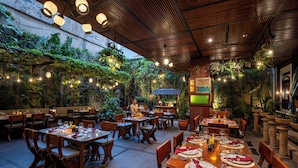An outdoor restaurant with wooden tables and chairs, surrounded by lush greenery and plants. - Rama Residence Padma (Legian)