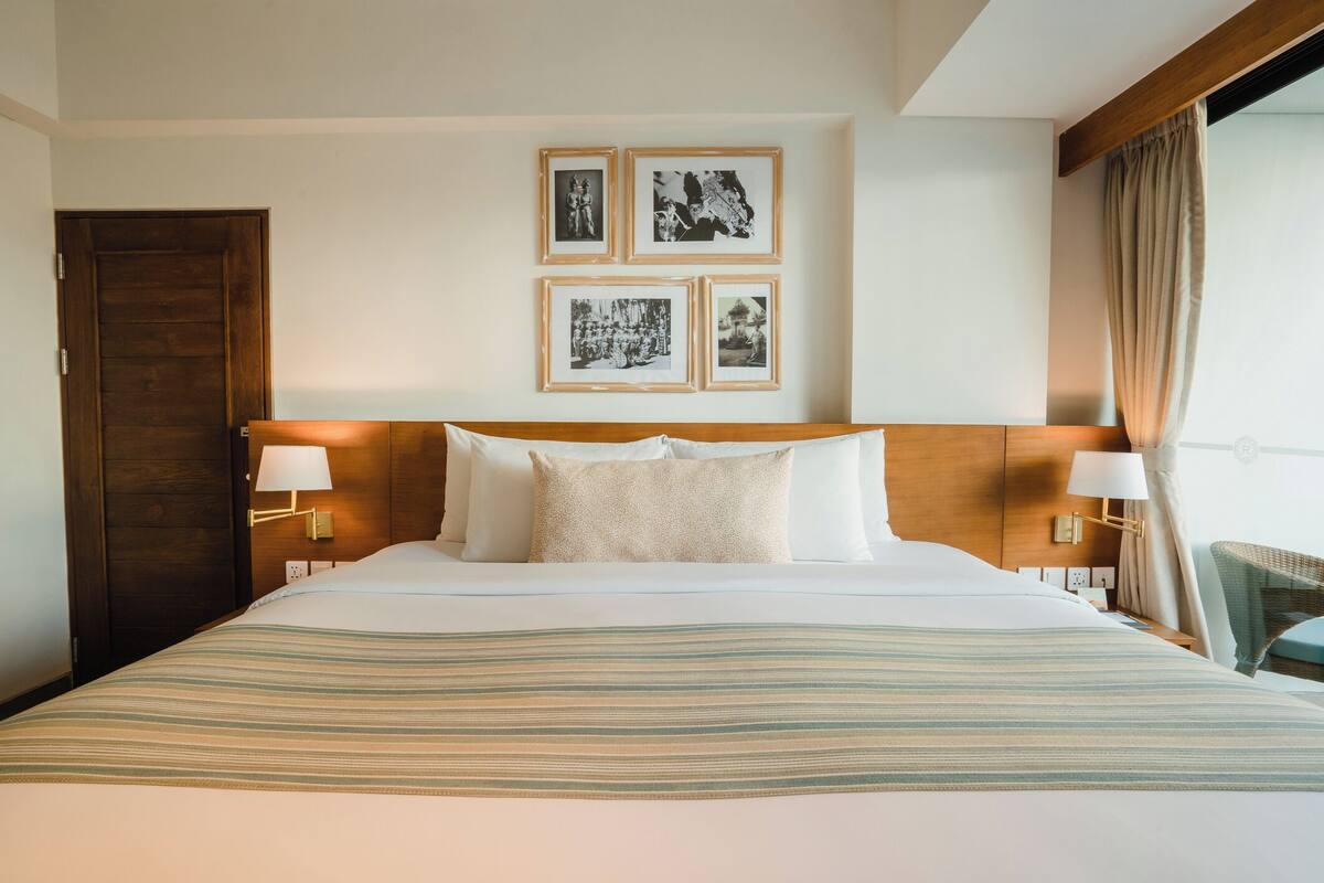 Une chambre d’hôtel avec un grand lit, une tête de lit en bois, une table de chevet avec une lampe et un mur orné de tableaux.