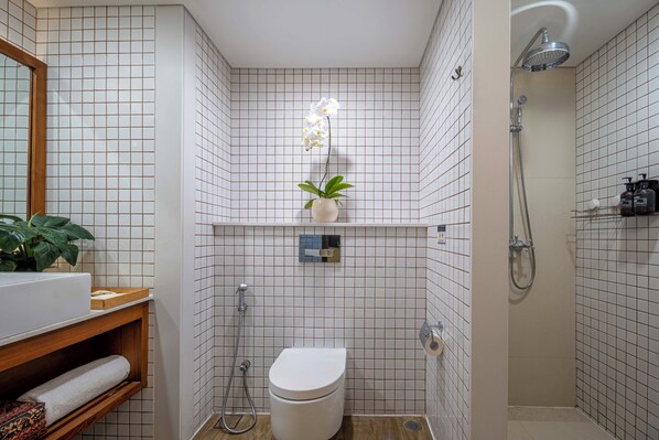 A bathroom with a toilet, a shower, a sink, and a mirror. - Rama Residence Padma (Legian)
