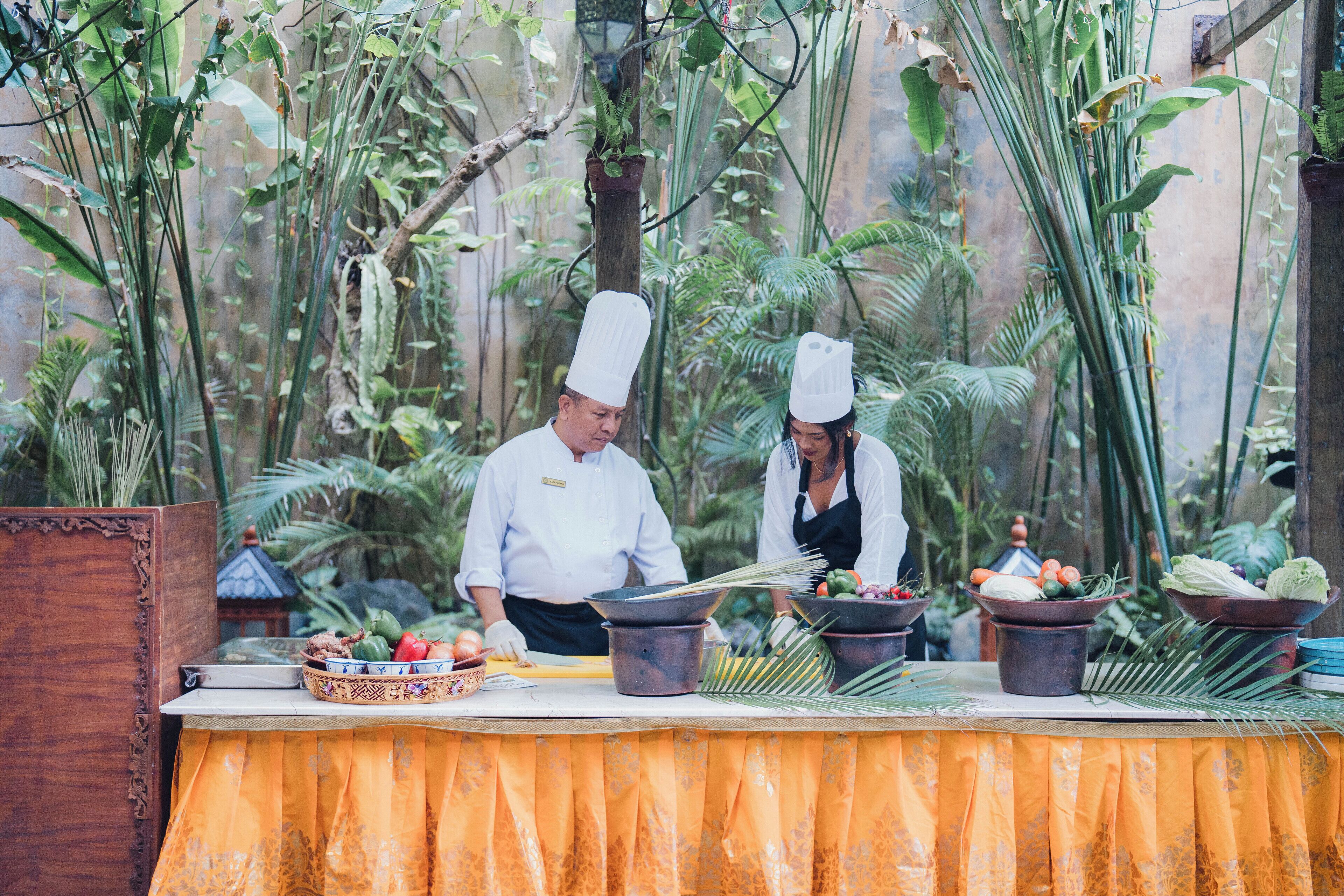A chef preparing food outdoors with a tropical backdrop.