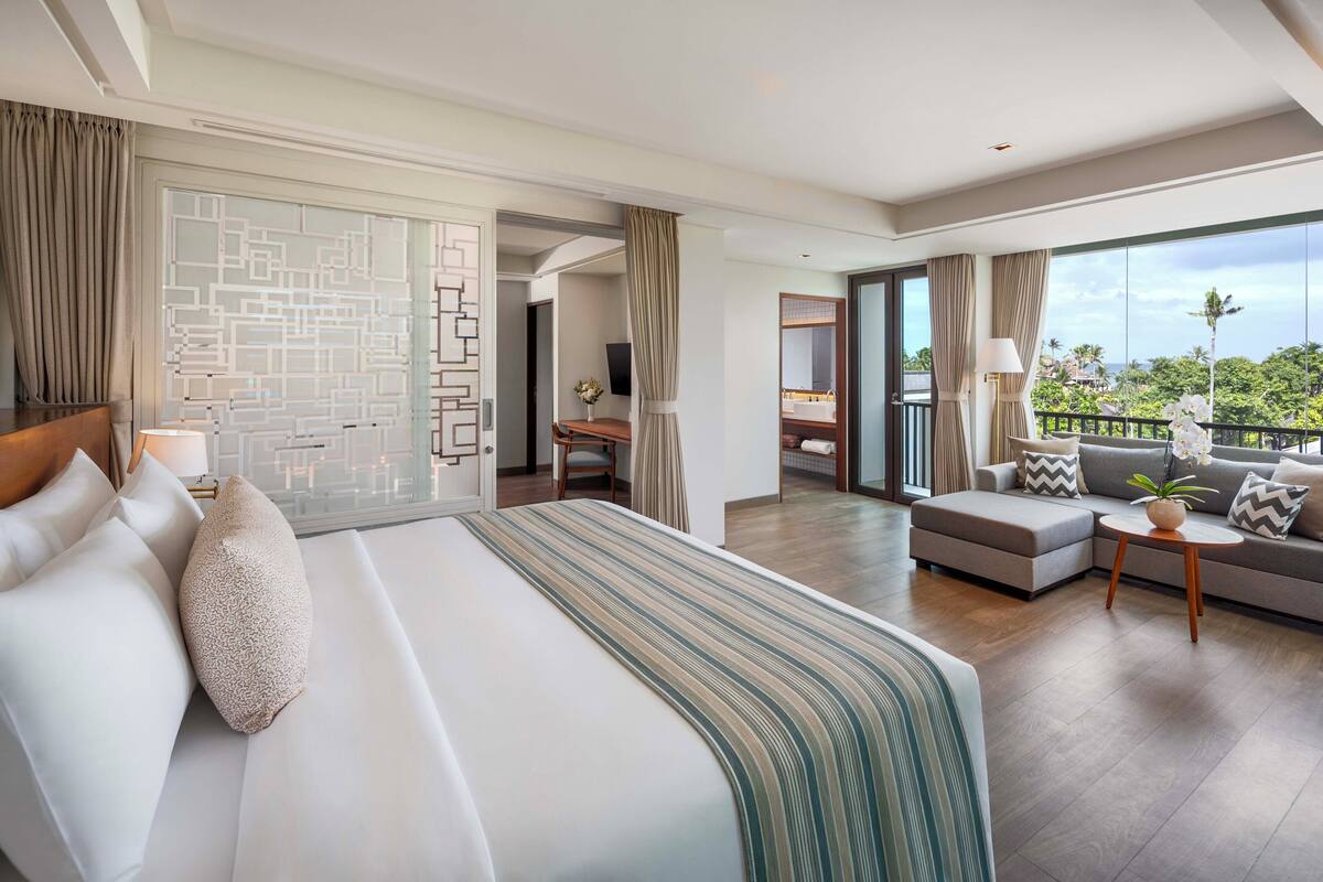 Une chambre d’hôtel avec un grand lit, un canapé, une petite table et un balcon avec vue.