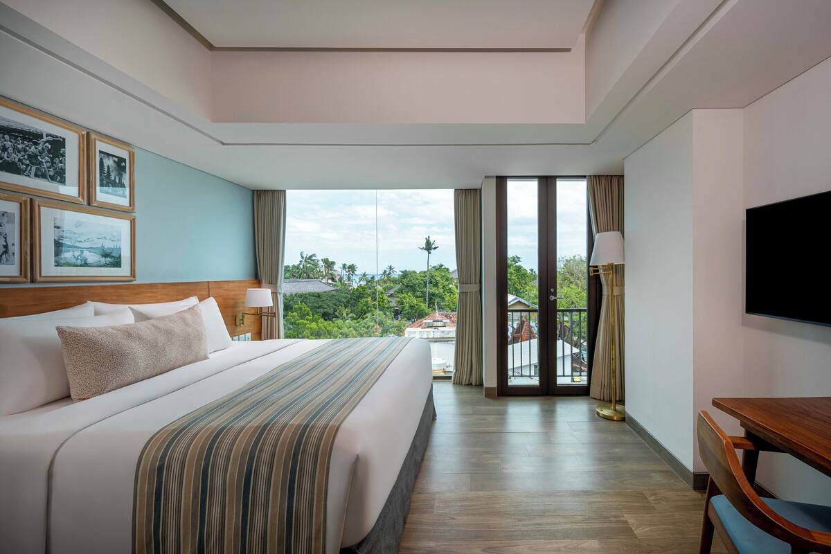 Une chambre d’hôtel avec un grand lit, une télévision, un bureau et un balcon donnant sur un espace verdoyant.