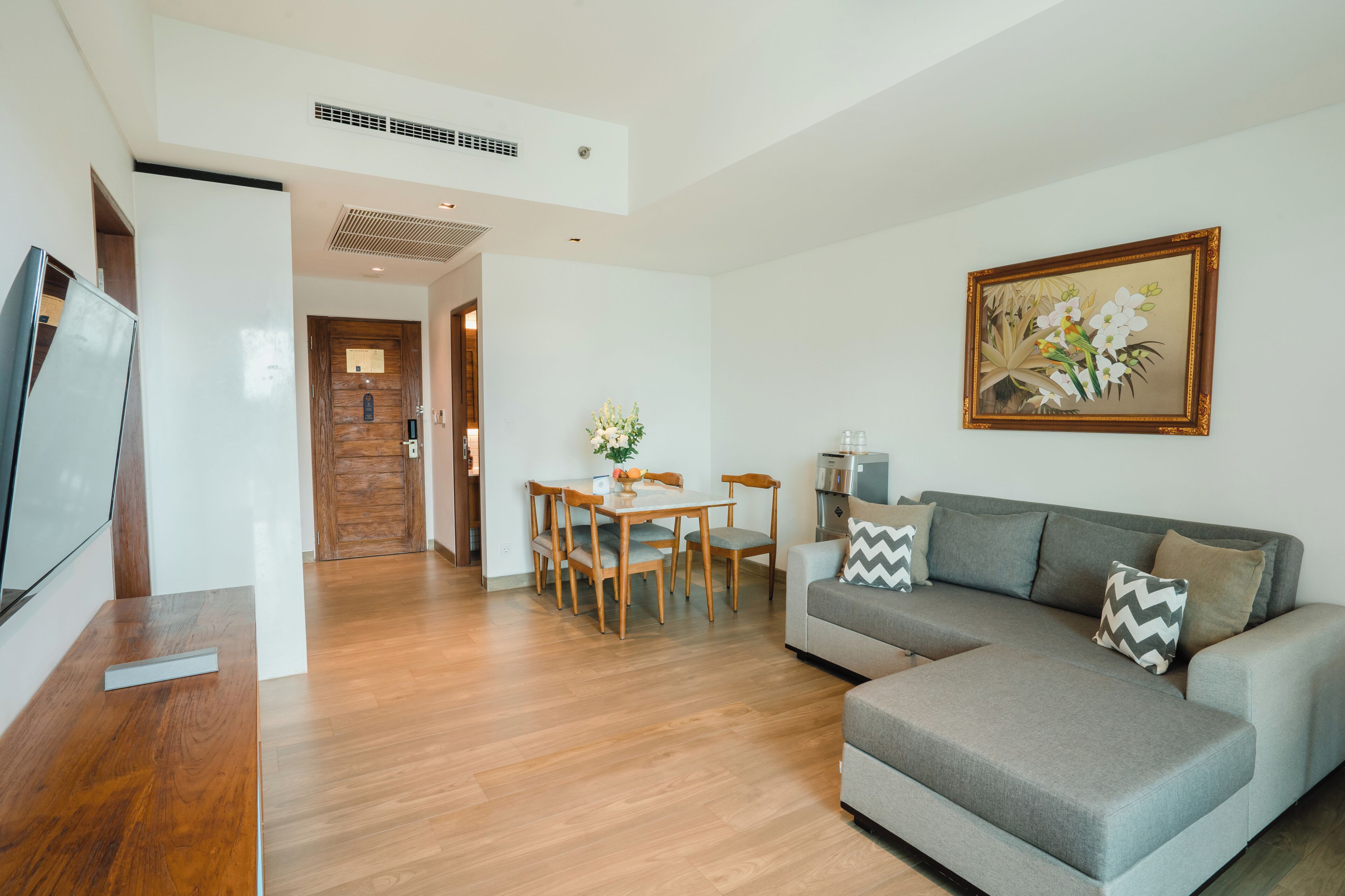 A modern living room with a grey sofa, wooden dining table, and a painting on the wall.