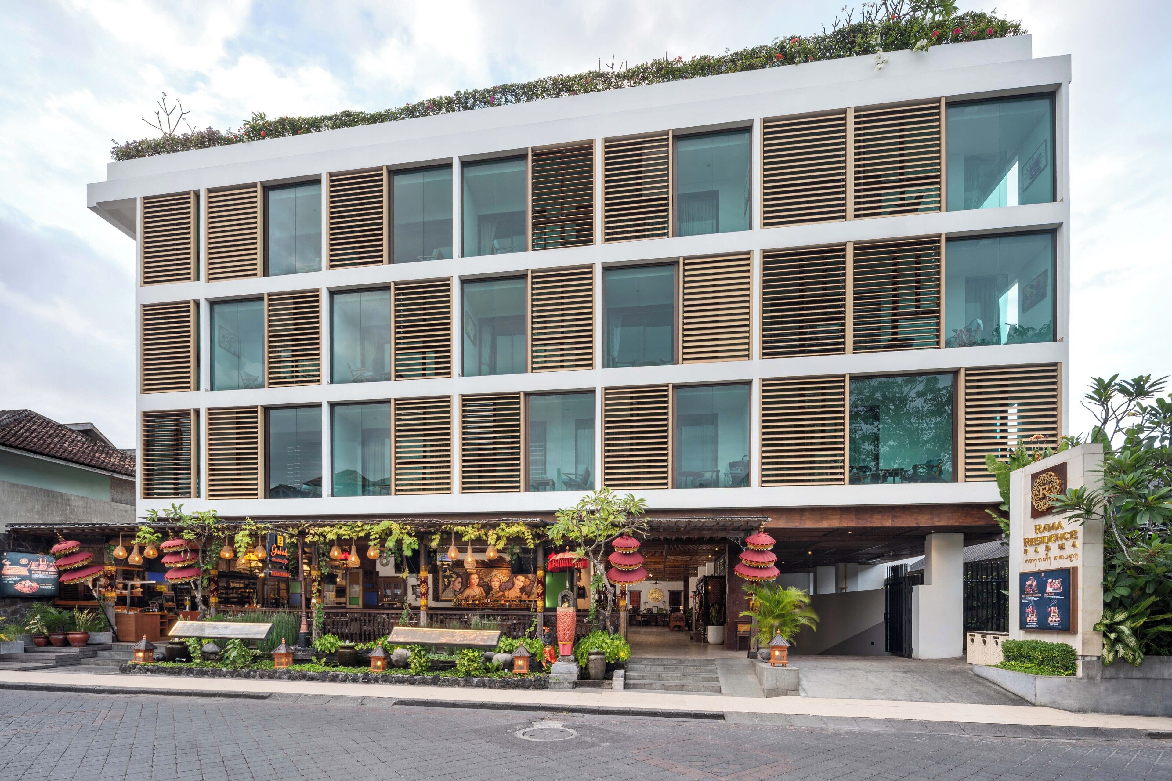 A modern building with multiple floors, large windows, and a covered entrance area with plants and decorative elements.