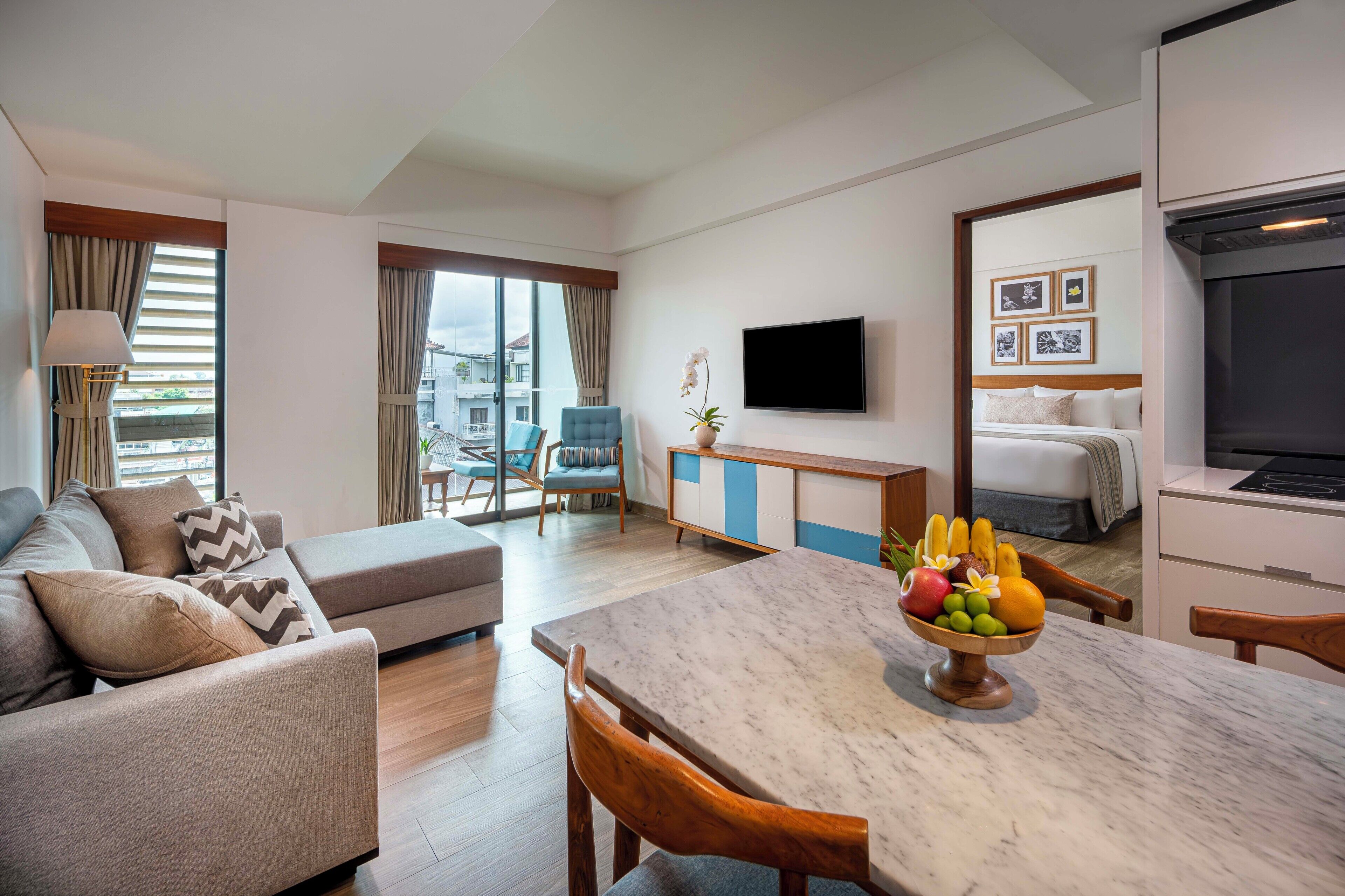 A modern hotel room with a living area, dining table, and a bed.