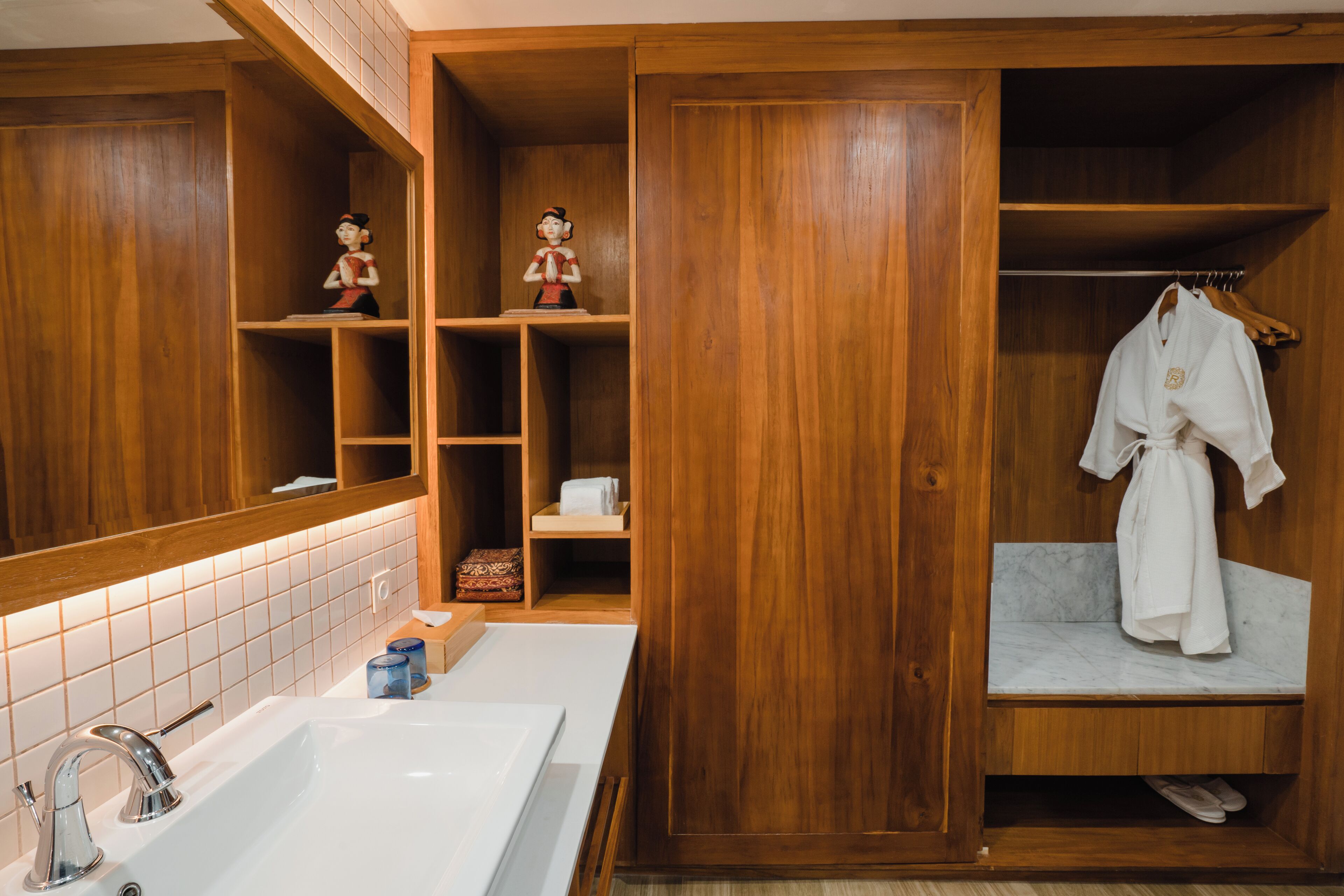 A wooden bathroom with a large mirror, a sink, shelves with toiletries, and a robe hanging on a rack.
