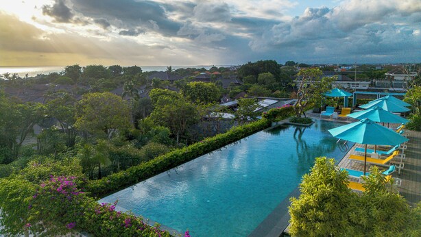 A resort pool with a view of the ocean, surrounded by lush greenery and a cloudy sky. - Rama Residence Padma (Legian)