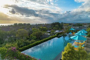 Ein Hotelpool mit Blick auf den Ozean, umgeben von üppiger Vegetation und einem bewölkten Himmel.