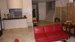 A hotel lobby with a reception desk, a red sofa, a staircase, and a brick wall.