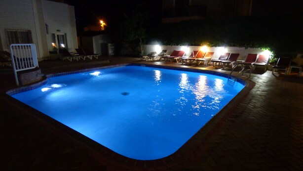 A swimming pool with a tiled edge, surrounded by lounge chairs and a brick walkway.