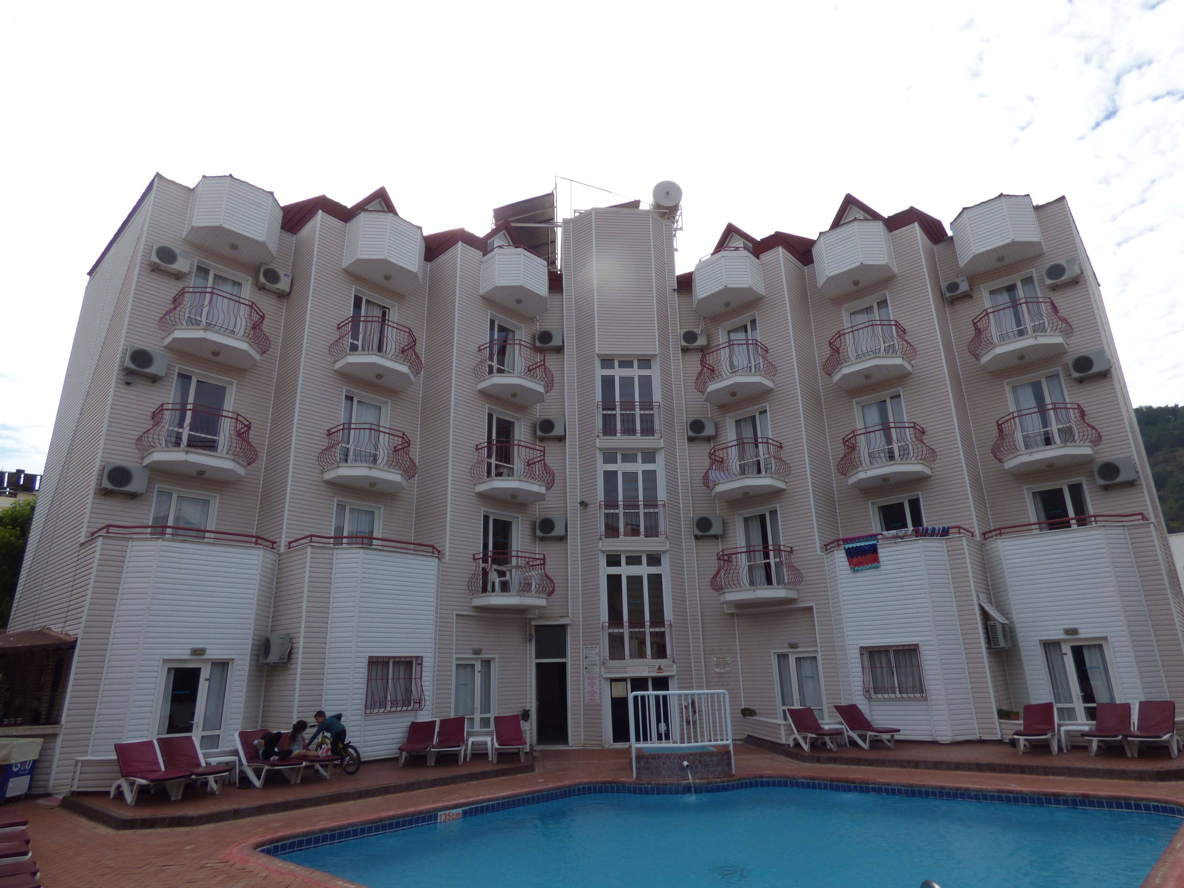 A multi-story hotel with balconies, a swimming pool, and lounge chairs.