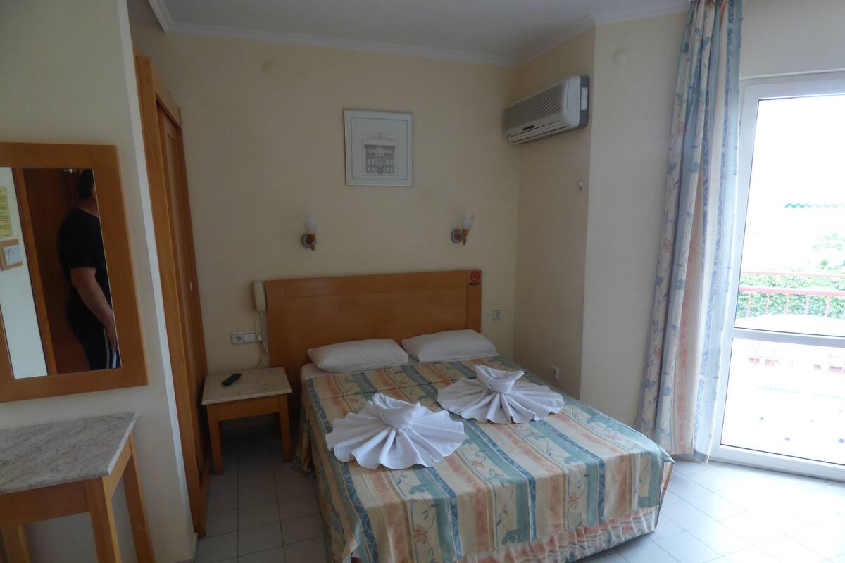 A hotel room with a bed, bedside table, and a mirror.