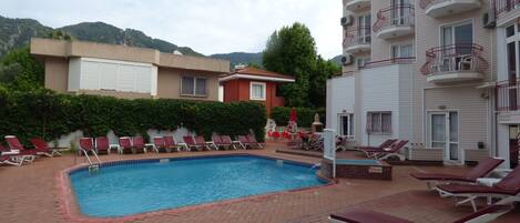 A swimming pool with sun loungers and a red-tiled deck.