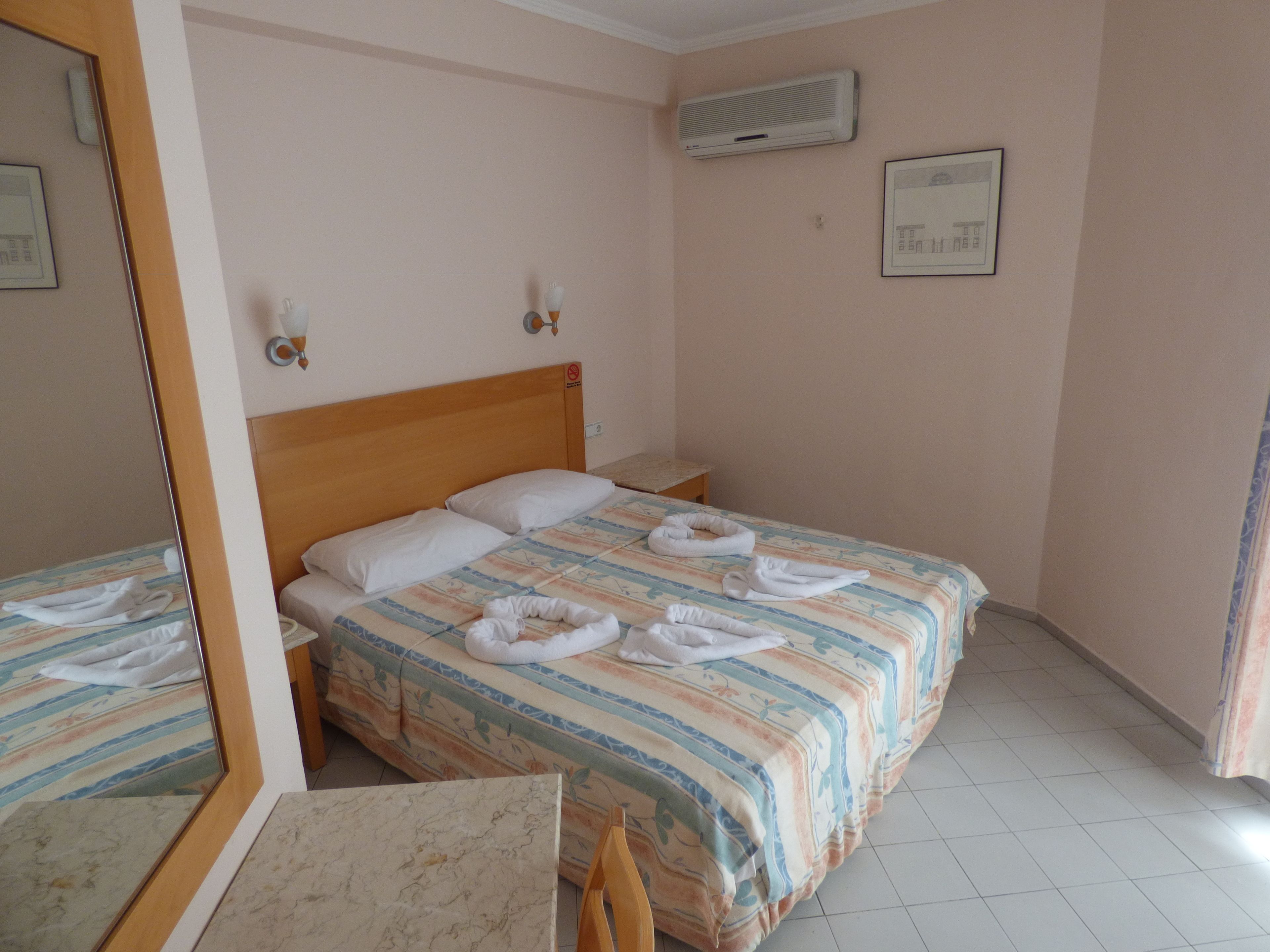 A hotel room with a bed, a nightstand, a mirror, and a window with curtains.