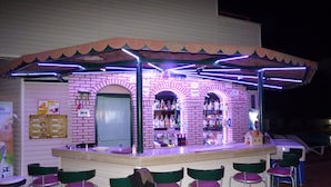 A bar with a brick facade, a counter with stools, and a variety of bottles on shelves.